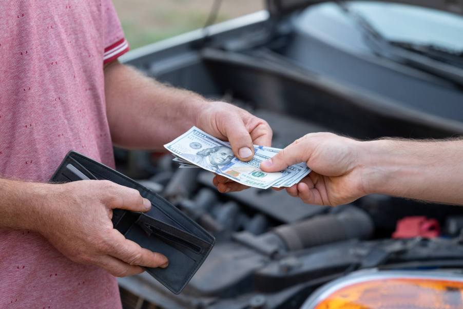 Handing a mechanic cash with car behind in close view of their hands