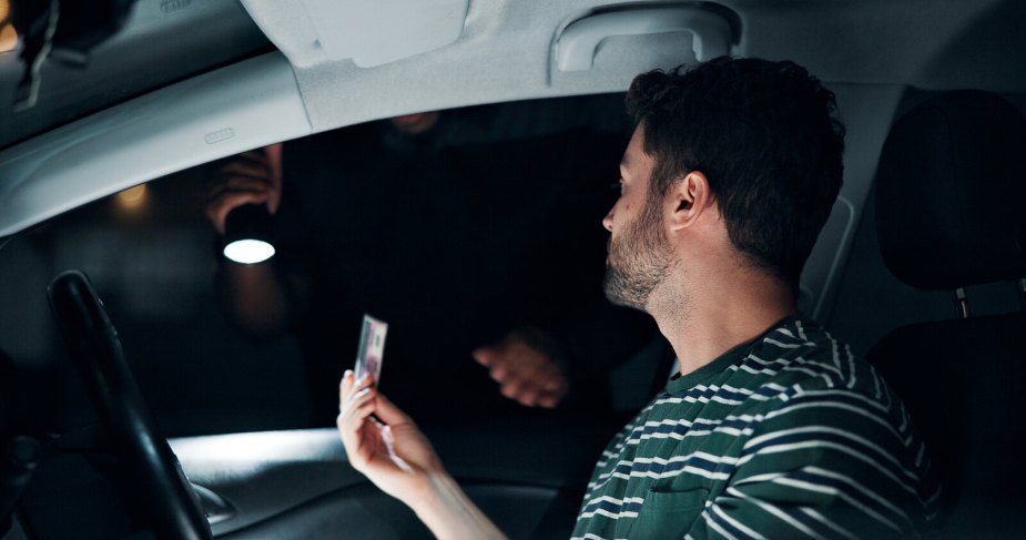 A driver hands a police officer their license at night