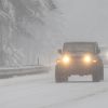 A Jeep with its headlights on drives on a snowy highway