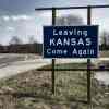 A road sign reading "Leaving Kansas Come Again"