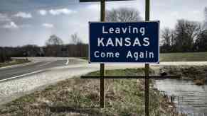 A road sign reading "Leaving Kansas Come Again"