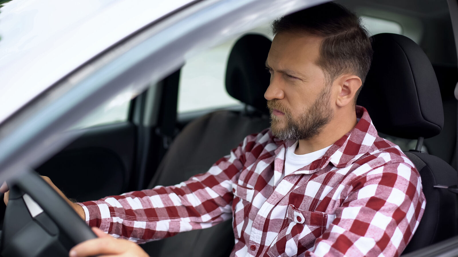 A male driver sits with hands on wheel with a wary look