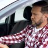 A male driver sits with hands on wheel with a wary look