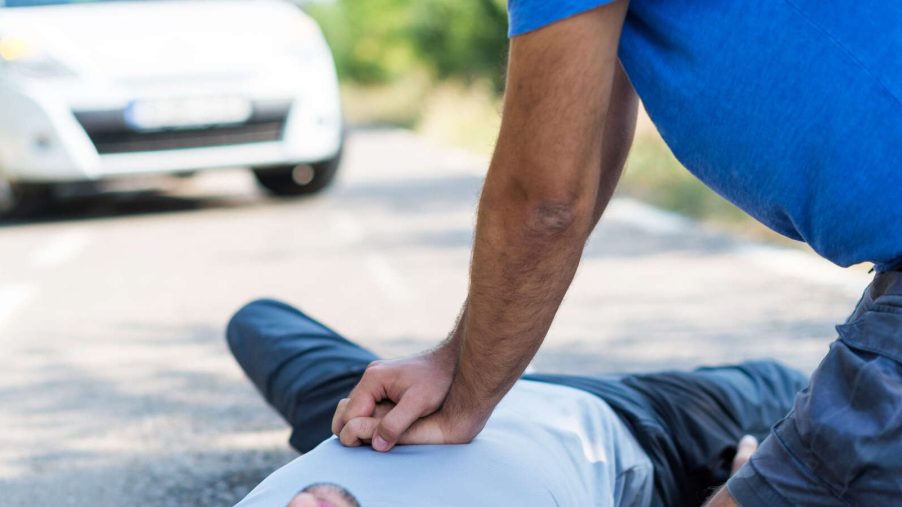 A man gives a driver CPR in front of a car