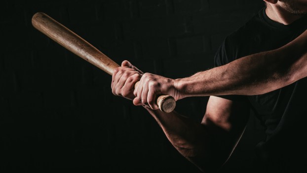 A man holding a baseball bat ready to swing with shadowed black background
