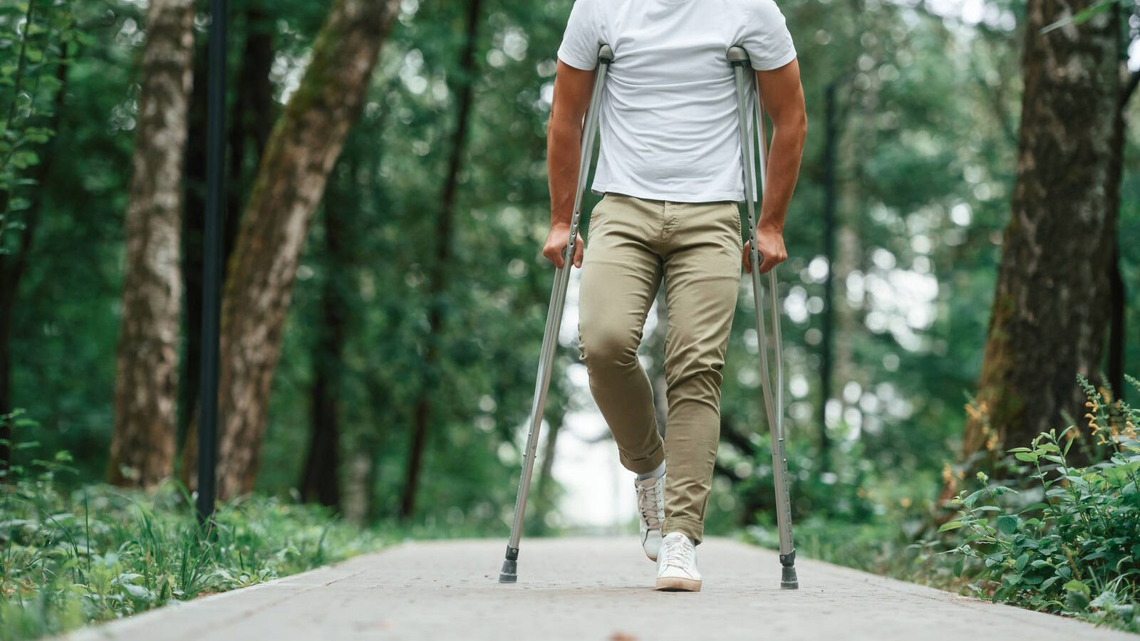 A man standing with crutches on a wooded paved path