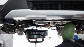 A mechanic drains car oil facing away from viewer