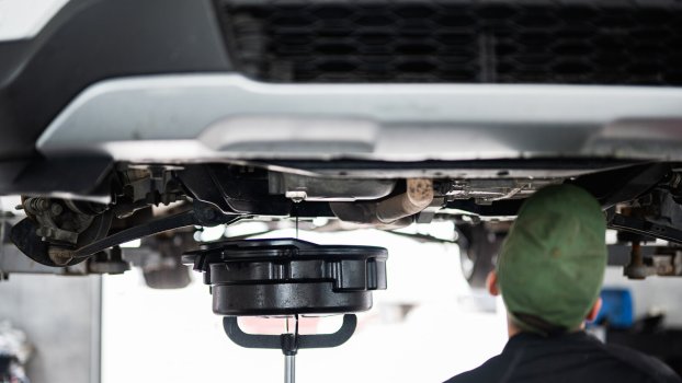 A mechanic drains car oil facing away from viewer