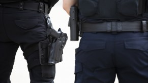 Two police officers standing facing away from viewer from torso to mid-thighs