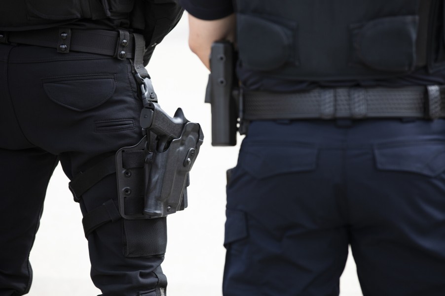 Two police officers standing facing away from viewer from torso to mid-thighs