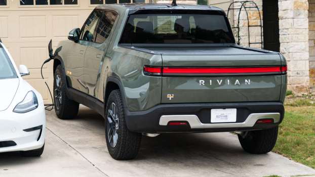 A green Rivian EV truck charging in a residential driveway next to a white Tesla