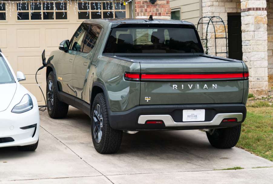 A green Rivian EV truck charging in a residential driveway next to a white Tesla