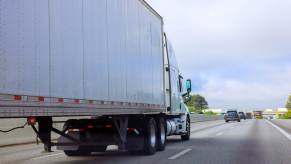 A semi-truck driving on a highway in right rear angle view