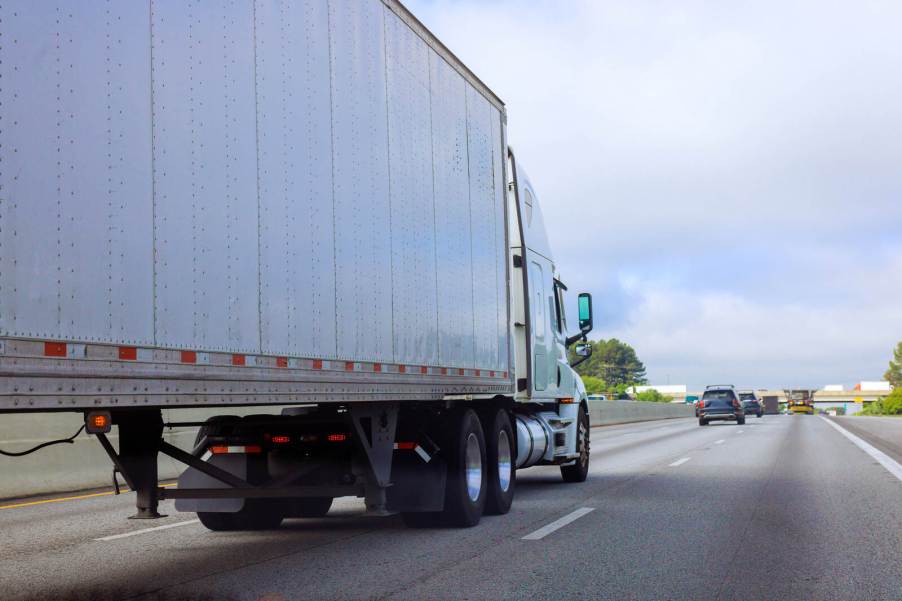 A semi-truck driving on a highway in right rear angle view