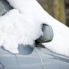 A light blue metallic car covered in snow in close right front view
