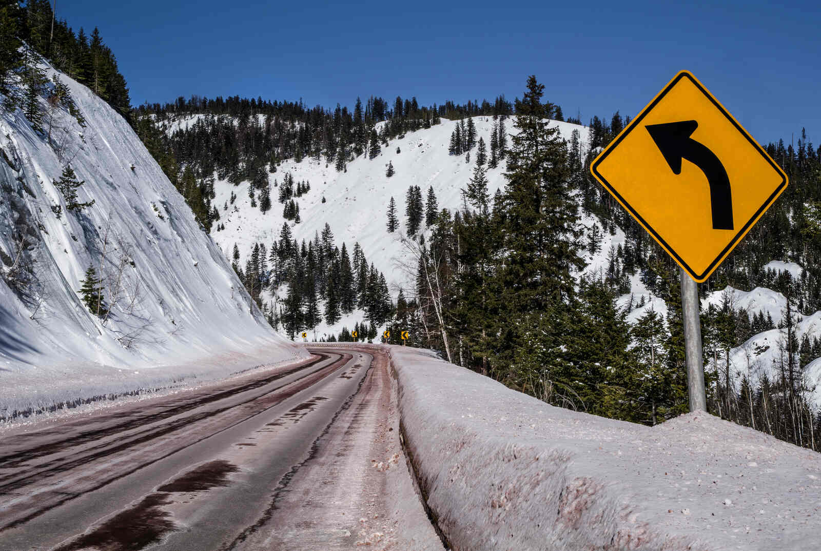 A "left curve" sign on a snowy mountain highway