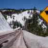A "left curve" sign on a snowy mountain highway