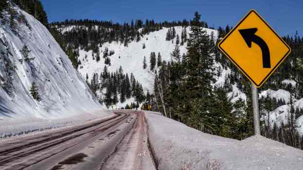 A "left curve" sign on a snowy mountain highway
