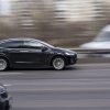 A black Tesla driving fast on a highway in right profile view