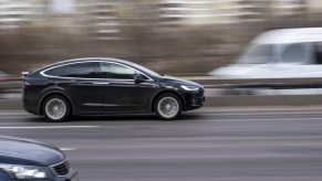 A black Tesla driving fast on a highway in right profile view