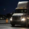 A white semi-truck parked in left front angle view at night in front of traffic barrels