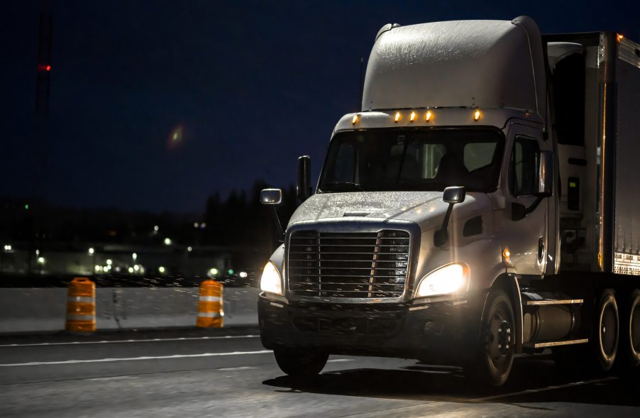 A white semi-truck parked in left front angle view at night in front of traffic barrels
