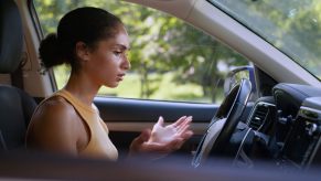 A worried female driver sits with palms open gesturing at car's performance issue