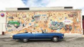 Blue Cadillac convertible parked in front of a mural on the side of a California store.