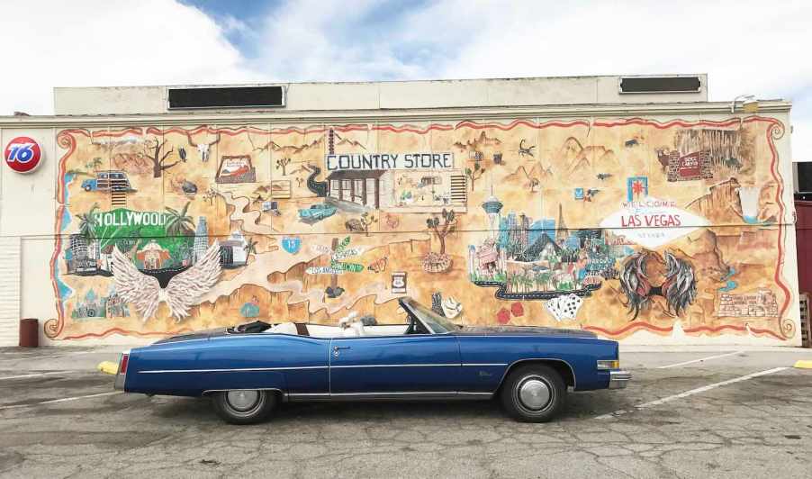 Blue Cadillac convertible parked in front of a mural on the side of a California store.