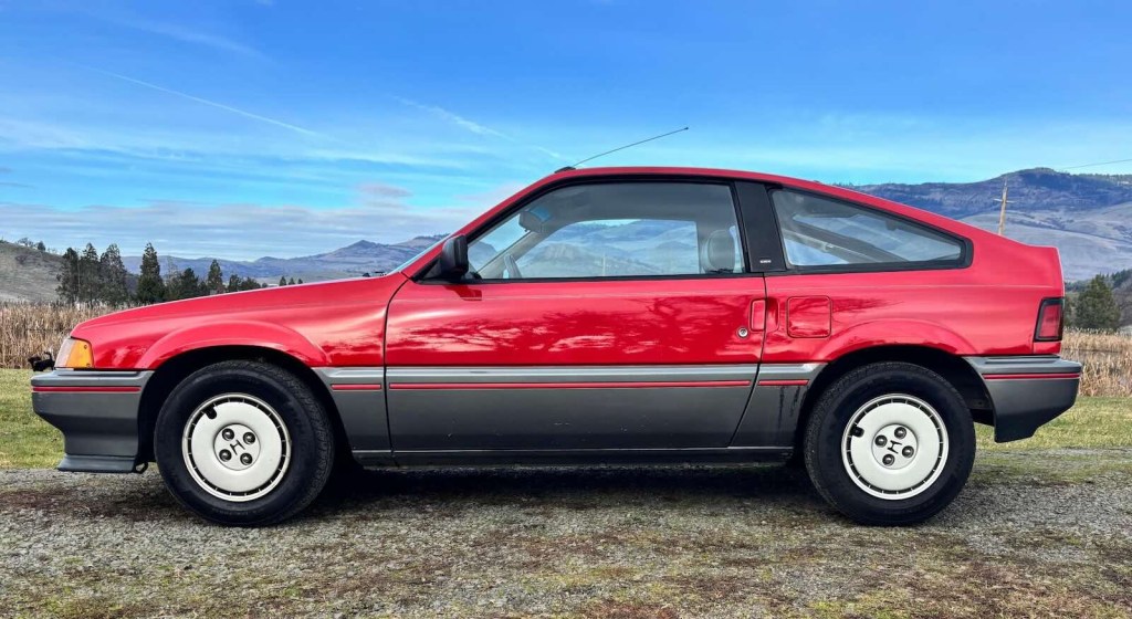 Silhouette of a red, compact, Honda Civic CRX, mountains visible in the background.