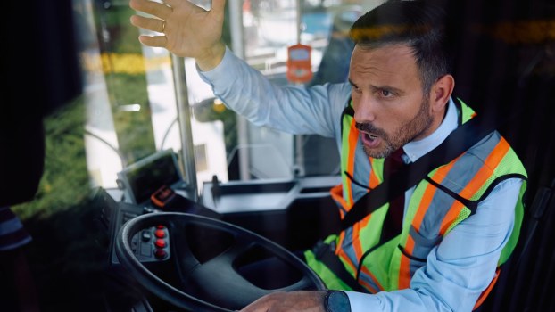 Angry bus driver gestures with one hand while steering with the other.