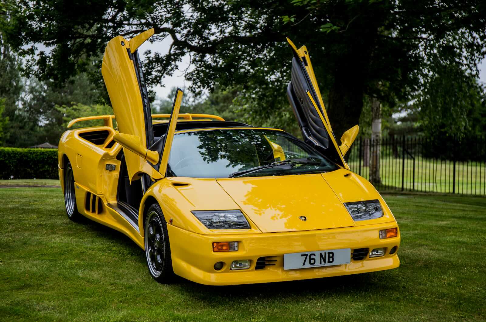 Bright yellow Lamborghini Diablo supercar with its doors up, parked on a grass field.