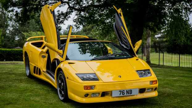 Bright yellow Lamborghini Diablo supercar with its doors up, parked on a grass field.