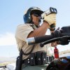 California Highway Patrol police officer standing over his motorcycle and holding a radar gun to detect speeders, blue sky visible behind him.