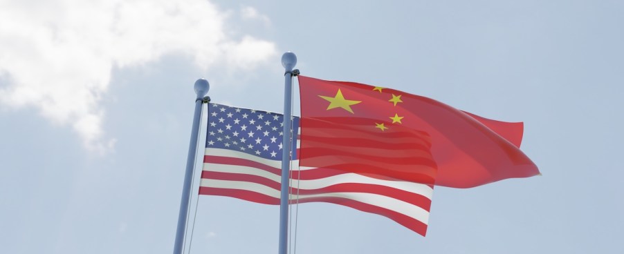The national flags of China (Front) and USA (rear) wave against the blue sky, white clouds in the background.