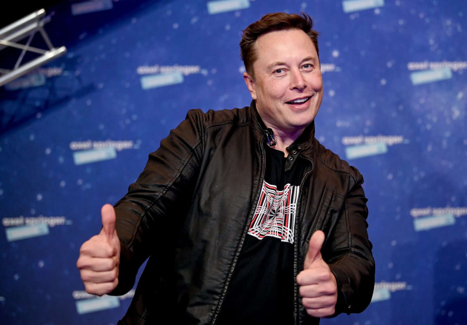 Tesal CEO Elon Musk smiles and gives a thumbs-up, on stage at an event