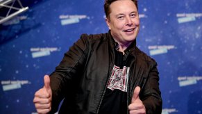 Tesal CEO Elon Musk smiles and gives a thumbs-up, on stage at an event