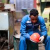 Worker sits in factory after layoffs, his orange helmet in his hands.