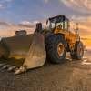 Front loader construction equipment parked in a sand pit, the sunsetting in the background.