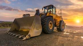 Front loader construction equipment parked in a sand pit, the sunsetting in the background.