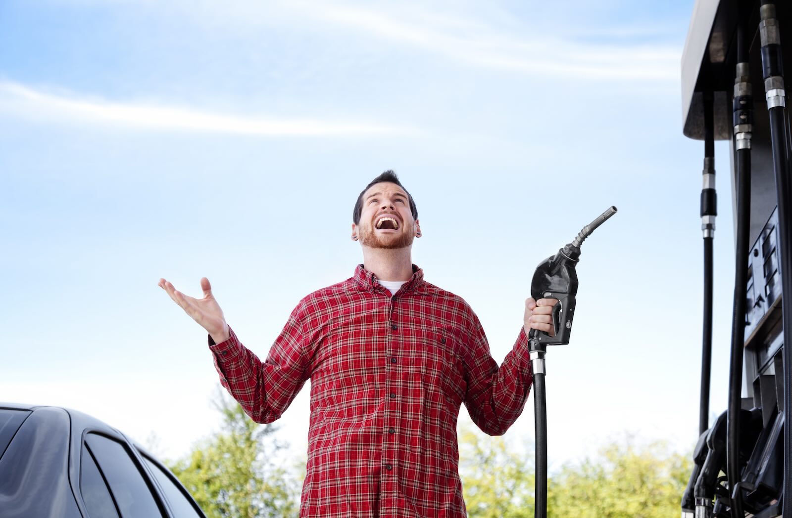 Man in flannel shirt holds up his hands with joy while fueling up at a gas station with discounts.
