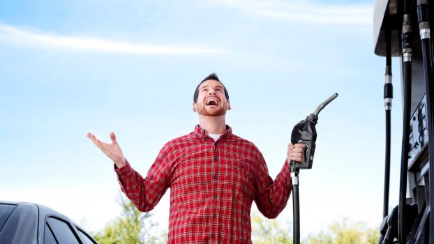 Man in flannel shirt holds up his hands with joy while fueling up at a gas station with discounts.