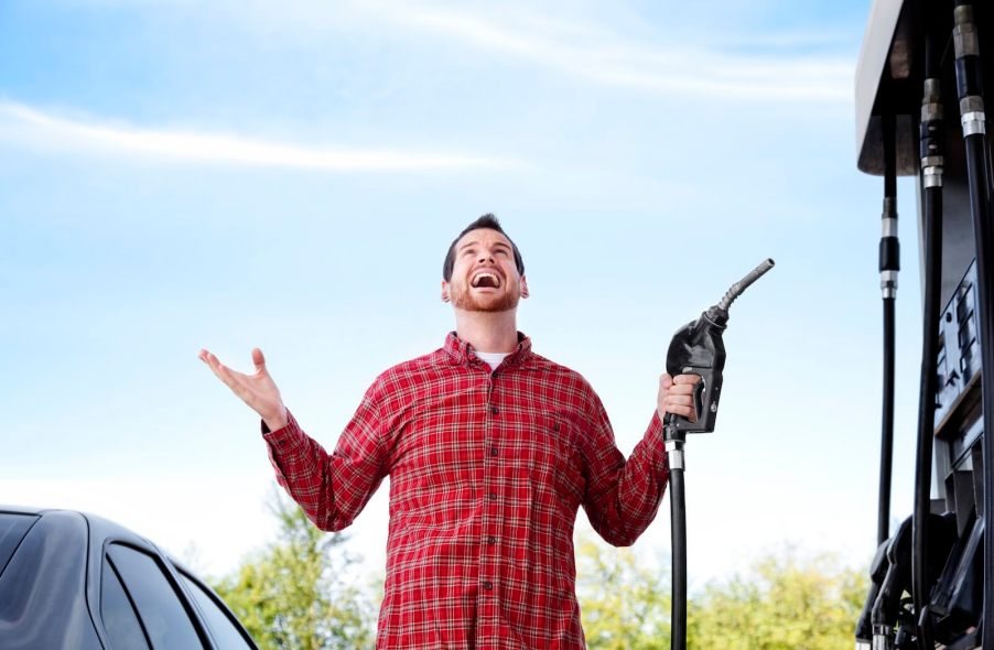Man in flannel shirt holds up his hands with joy while fueling up at a gas station with discounts.