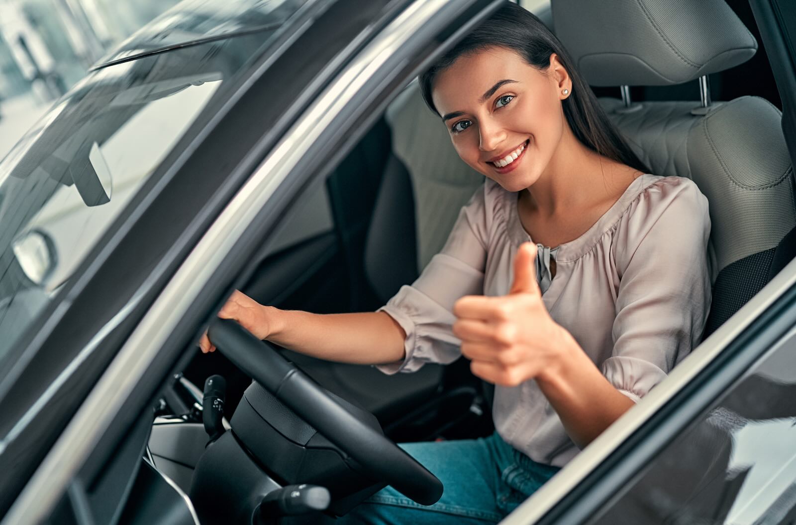 Young woman gives a thumbs up from the driver's seat of her reliable used car.