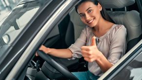 Young woman gives a thumbs up from the driver's seat of her reliable used car.