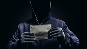 Hooded man holds envelope of stolen mail during identity theft scam.