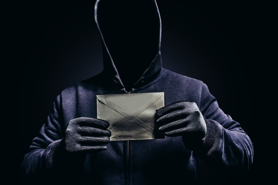 Hooded man holds envelope of stolen mail during identity theft scam.