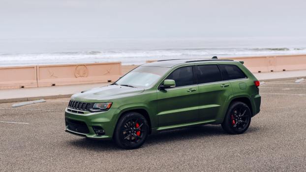 Green Jeep parked in front of the ocean.