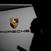 Man stands in front of the Porsche logo at an auto show.