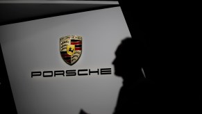 Man stands in front of the Porsche logo at an auto show.